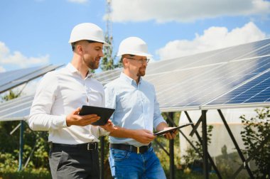 Güneş çiftliği (güneş paneli), iki mühendis ile birlikte sistemin işleyişini kontrol etmek için yürür, dünyanın enerjisini korumak için alternatif enerji, temiz enerji üretimi için fotovoltaik modül fikri.