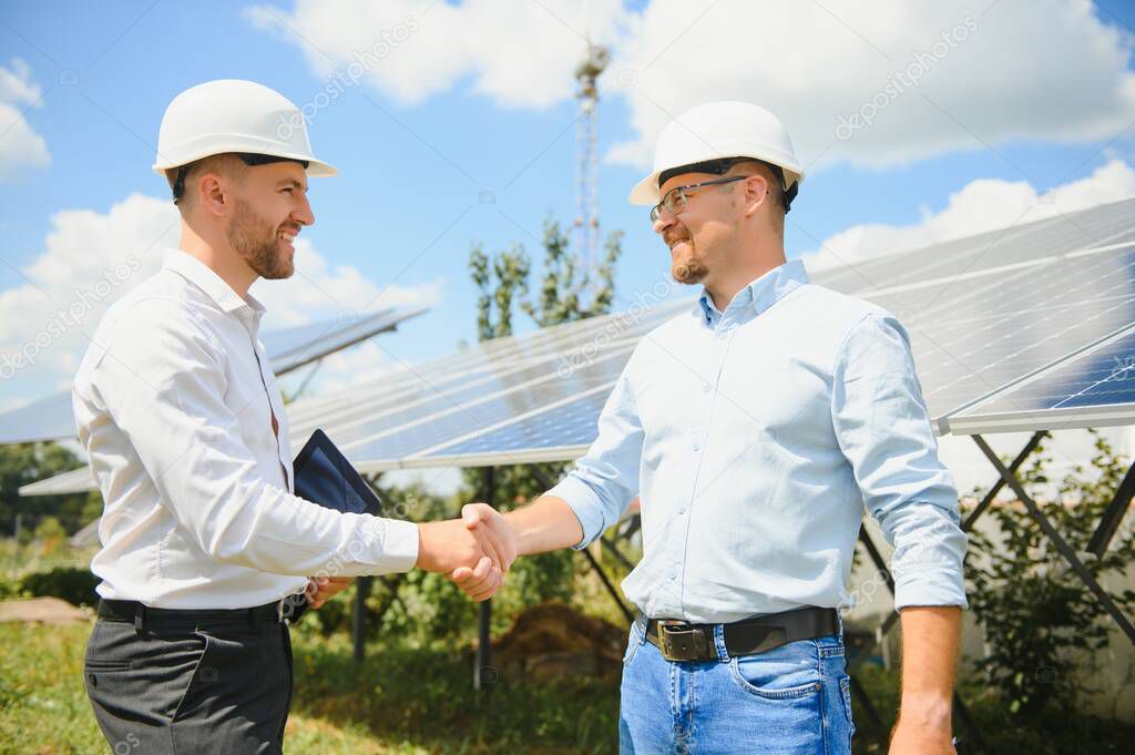 Workers shaking hands on a background of solar panels on solar power plant.