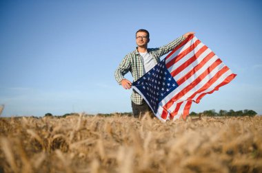 Buğday tarlasında dikilen Amerikan bayrağını tutan genç adam