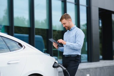 Adam şarj istasyonunda bir elektrikli arabayı şarj ediyor..