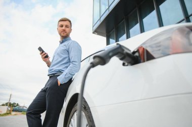 Adam şarj istasyonunda bir elektrikli arabayı şarj ediyor..