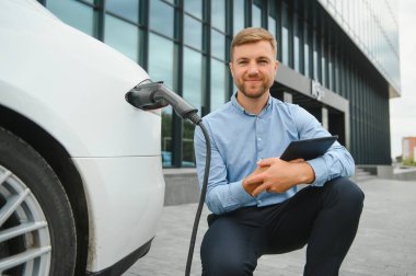 Adam şarj istasyonunda bir elektrikli arabayı şarj ediyor..