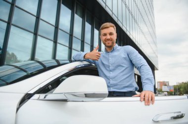 handsome young businessman standing near his car outdoors