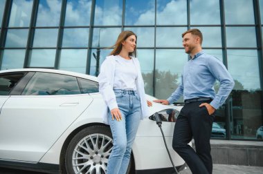 Smiling man and woman on the charging station for electric cars. A man is charging a car