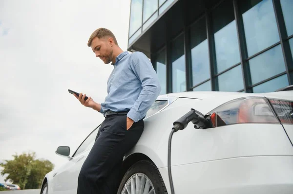 Man Charging His Electric Car Charge Station Using Smartphone — Stockfoto