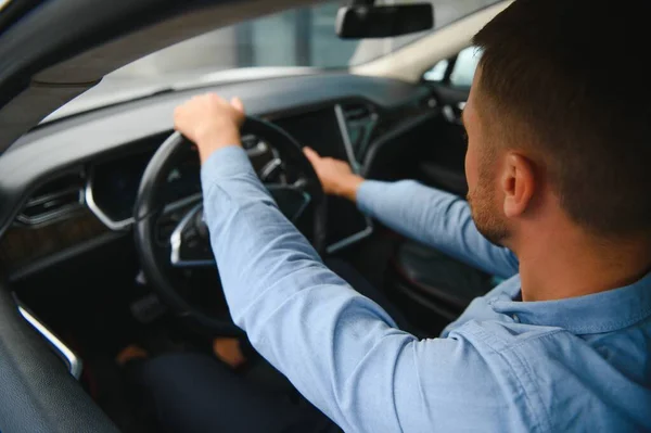 Man of style and status. Handsome young man in full suit smiling while driving a car