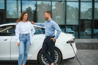 Smiling man and woman on the charging station for electric cars. A man is charging a car