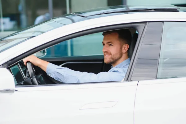 Man of style and status. Handsome young man in full suit smiling while driving a car