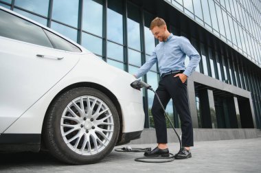 Adam şarj istasyonunda bir elektrikli arabayı şarj ediyor..