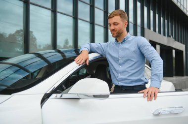 handsome young businessman standing near his car outdoors