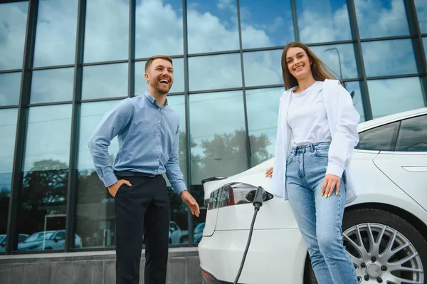 Smiling man and woman on the charging station for electric cars. A man is charging a car