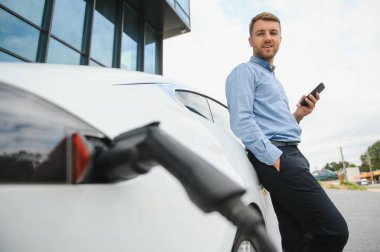 Adam şarj istasyonunda bir elektrikli arabayı şarj ediyor..