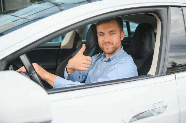 Man of style and status. Handsome young man in full suit smiling while driving a car