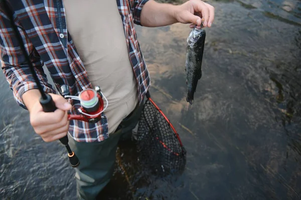 Fly-fisherman holding trout out of the water.