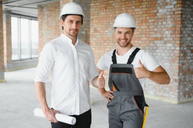 Engineer and worker checking project at building site background, construction site at sunset in evening time.