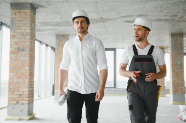 Engineer and worker checking project at building site background, construction site at sunset in evening time.