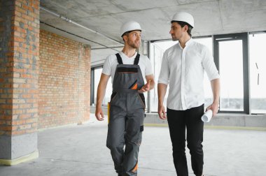 Engineer and worker checking project at building site background, construction site at sunset in evening time.
