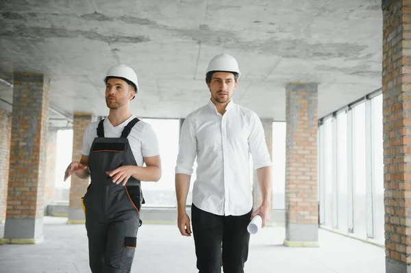 Engineer and worker checking project at building site background, construction site at sunset in evening time.