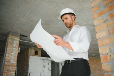 Portrait of man architect at building site. Confident construction manager wearing hardhat. Successful mature civil engineer at construction site with copy space