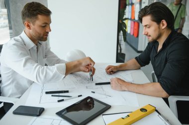 two people sit in front of construction plan and talk about the architecture.