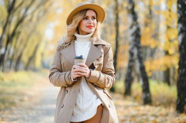 Young beautiful woman holding cup with coffee in the autumn park