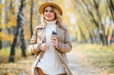 Young beautiful woman holding cup with coffee in the autumn park