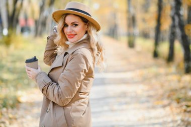 Young beautiful woman holding cup with coffee in the autumn park