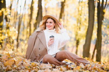 Young beautiful woman holding cup with coffee in the autumn park