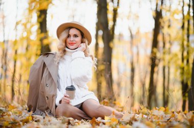 Young beautiful woman holding cup with coffee in the autumn park