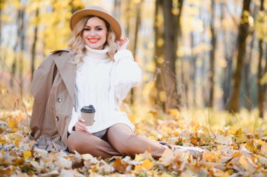 Young beautiful woman holding cup with coffee in the autumn park