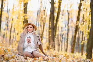 Young beautiful woman holding cup with coffee in the autumn park
