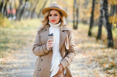 Kahve fincanı sonbahar parkta olan genç ve güzel kadın.