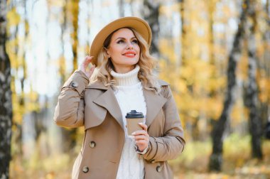 Young beautiful woman holding cup with coffee in the autumn park