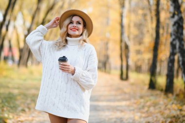 Young beautiful woman holding cup with coffee in the autumn park