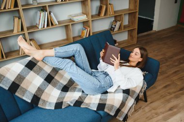 Young beautiful woman wearing white t-shirt on textile sofa at home. Attractive slim female in domestic situation, resting on couch in her lofty apartment. Background, copy space, close up