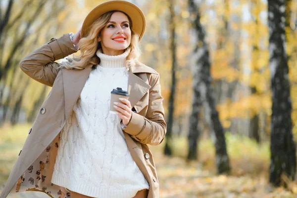Young beautiful woman holding cup with coffee in the autumn park