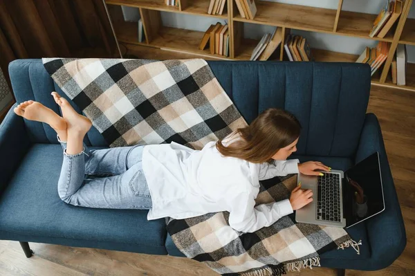 Young woman lying on couch with laptop