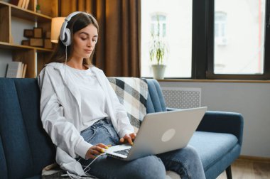 Kanepede oturup dizüstü bilgisayarla iletişim kuran mutlu genç kız bilgisayarda yazı yazan, blog yazmaktan ya da sosyal ağda arkadaşlarıyla sohbet etmekten keyif alan genç kadın..