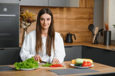 Mutlu gülümseyen tatlı kadın, evde bir sürü sebzeyle taze ve sağlıklı bir vegan salatası hazırlıyor ve yeni bir tarif deniyor..