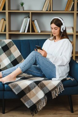 Beautiful young caucasian woman in casual clothing enjoying music and smiling while resting at home. Young woman with headphones using laptop at home.
