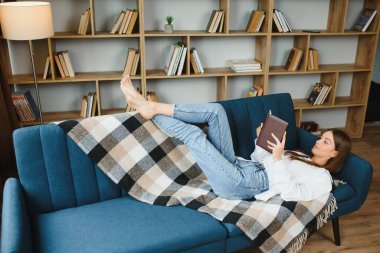 Young beautiful woman wearing white t-shirt on textile sofa at home. Attractive slim female in domestic situation, resting on couch in her lofty apartment. Background, copy space, close up