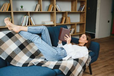 Young beautiful woman wearing white t-shirt on textile sofa at home. Attractive slim female in domestic situation, resting on couch in her lofty apartment. Background, copy space, close up