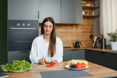 Mutlu gülümseyen tatlı kadın, evde bir sürü sebzeyle taze ve sağlıklı bir vegan salatası hazırlıyor ve yeni bir tarif deniyor..