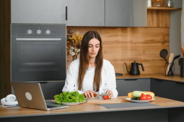 Athletic woman blogger nutritionist prepare a salad with fresh vegetables and conducts a video conference on healthy eating on laptop in the kitchen.