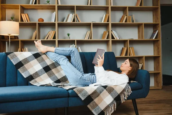 Young beautiful woman wearing white t-shirt on textile sofa at home. Attractive slim female in domestic situation, resting on couch in her lofty apartment. Background, copy space, close up