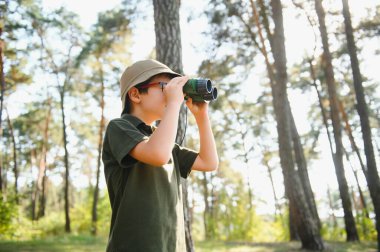 Little boy scout with binoculars during hiking in autumn forest. Concepts of adventure, scouting and hiking tourism for kids