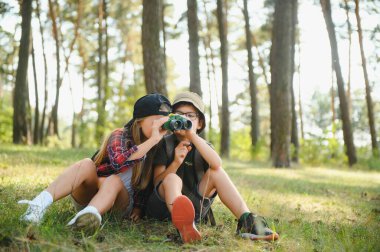 Two happy children having fun during forest hike on beautiful day in pine forest. Cute boy scout with binoculars during hiking in summer forest. Concepts of adventure, scouting and hiking tourism.
