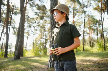 Boy with binoculars. Kid in green forest at summer daytime together