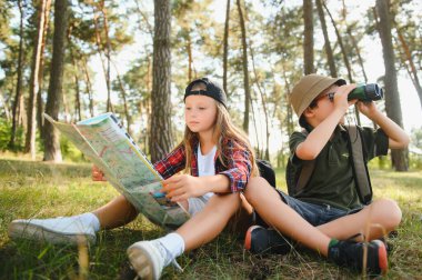 Two happy children having fun during forest hike on beautiful day in pine forest. Cute boy scout with binoculars during hiking in summer forest. Concepts of adventure, scouting and hiking tourism.