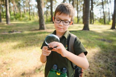 schoolboy is exploring nature with magnifying glass. Summer vacation for inquisitive kids in forest. Hiking. Boy-scout